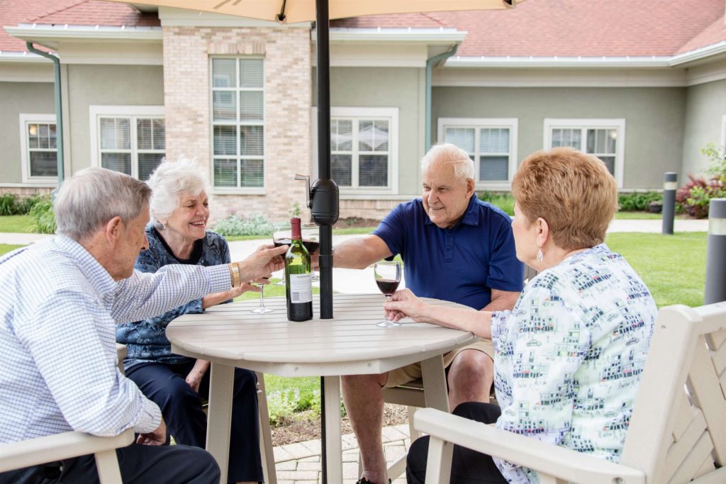 a group of older people drinking wine at an outdoor table.