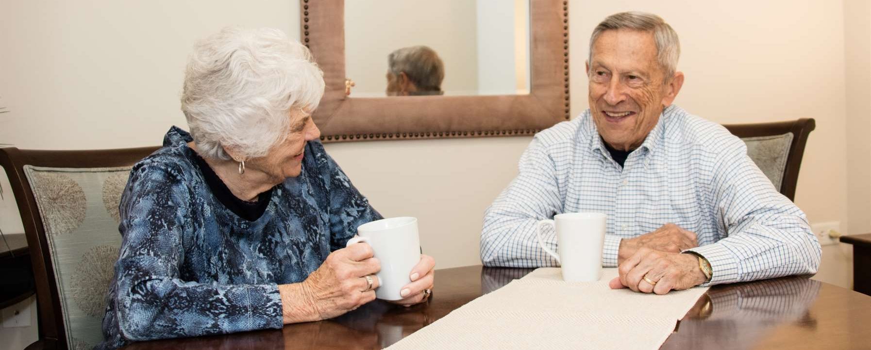 an older couple sitting at a table and drinking coffee.