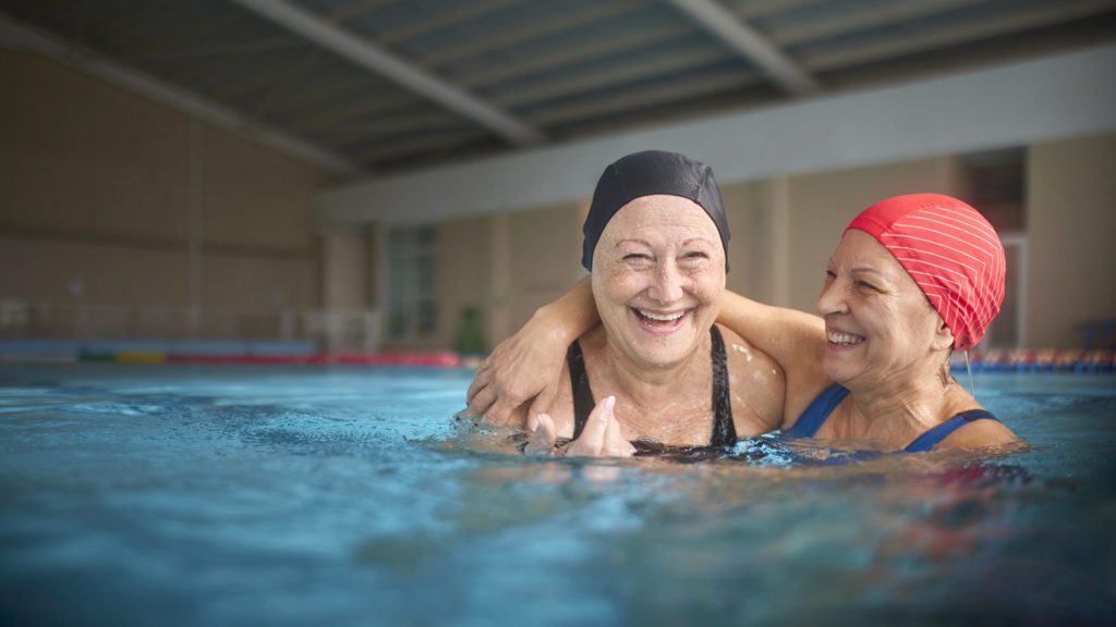 Two senior women embracing together in swimming indoor pool